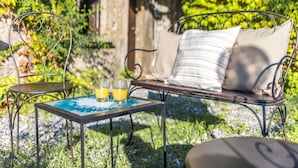 A metal outdoor seating area with a table and two chairs, a cushion, and two glasses of orange juice.