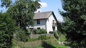 Ein zweistöckiges Haus mit weißer Fassade, grauem Dach und einem eingezäunten Garten.
