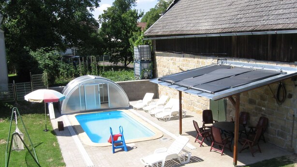 Ein Garten mit Swimmingpool, überdachter Terrasse und einem Steinhaus.