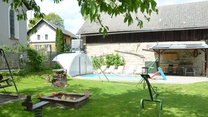 Ein Garten mit Schwimmbad, Gewächshaus und Gartenmöbeln.