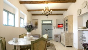 A dining area with a round table, chairs, a chandelier, and a television on the wall.