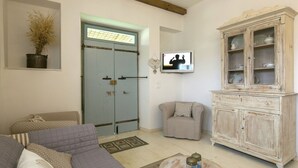 A living room with a sofa, armchair, wooden cabinet, and a television on the wall.