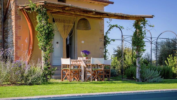 A poolside area with a table and chairs, a pergola, and a building with a brick wall and a door.