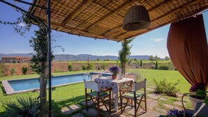 A poolside area with a table and chairs, surrounded by greenery and a view of distant hills.