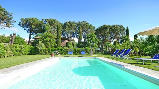 A clear blue pool with a tiled deck, surrounded by green hedges and trees. - Villa in Cortona With Pool & Countryside Views (Cortona)