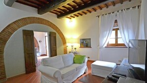 A cozy living room with a white sofa, a small table, a TV, and a fireplace. - Villa in Cortona With Pool & Countryside Views (Cortona)