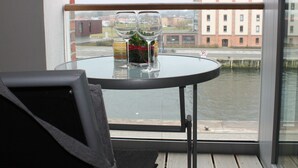 Un balcone con un tavolino in vetro, due bicchieri da vino e una bottiglia.