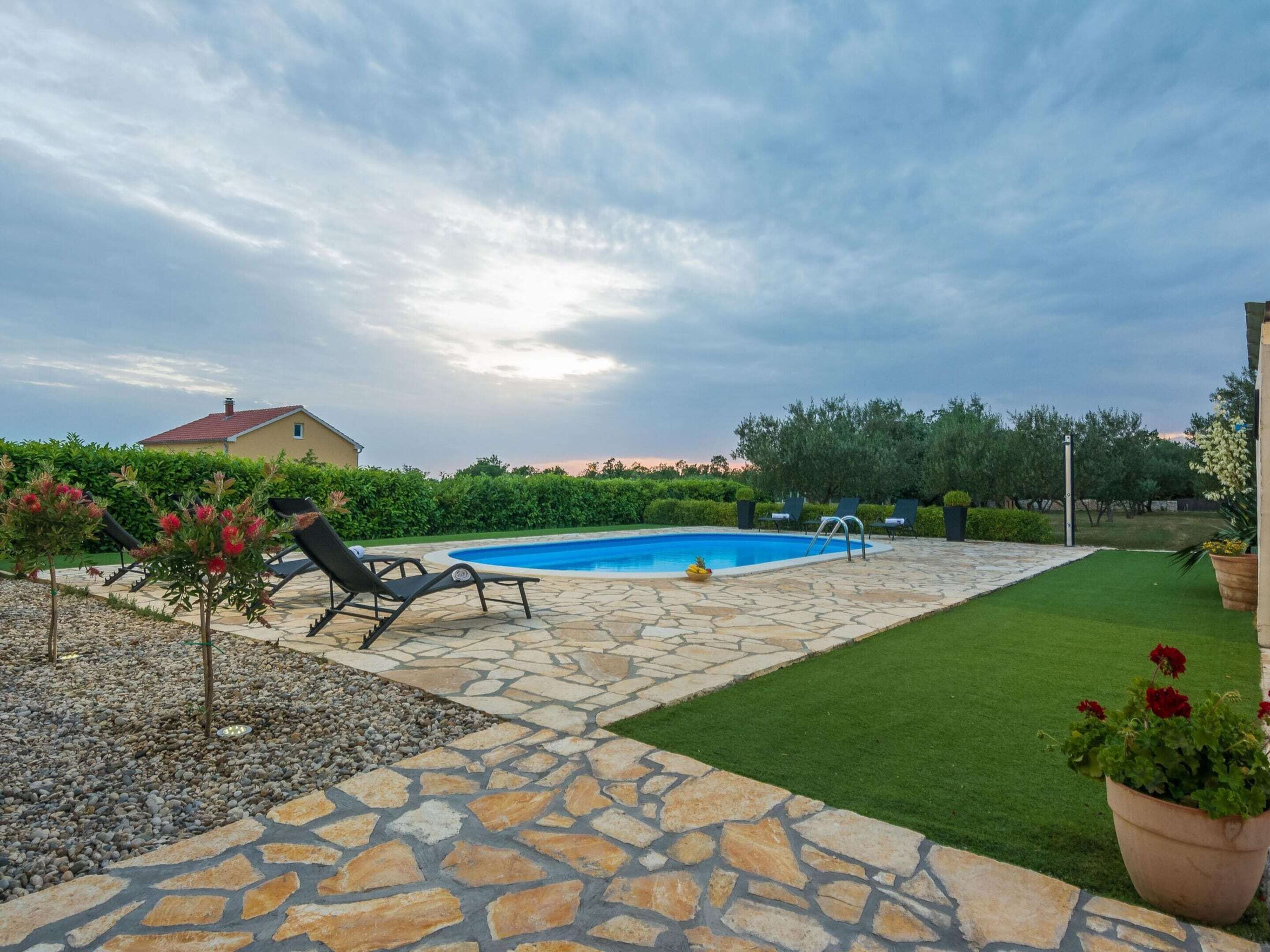 A backyard with a swimming pool, stone patio, and green lawn.