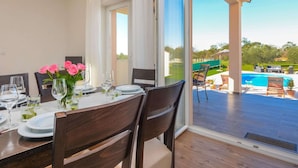 A dining area with a table set for four, large windows, and a view of a swimming pool. - Peaceful Home in Policnik (Policnik)