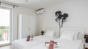 A hotel room with two beds, white bedding, a wardrobe, a ceiling air conditioner, a nightstand with a lamp, and a balcony with a railing. - Peaceful Home in Policnik (Policnik)