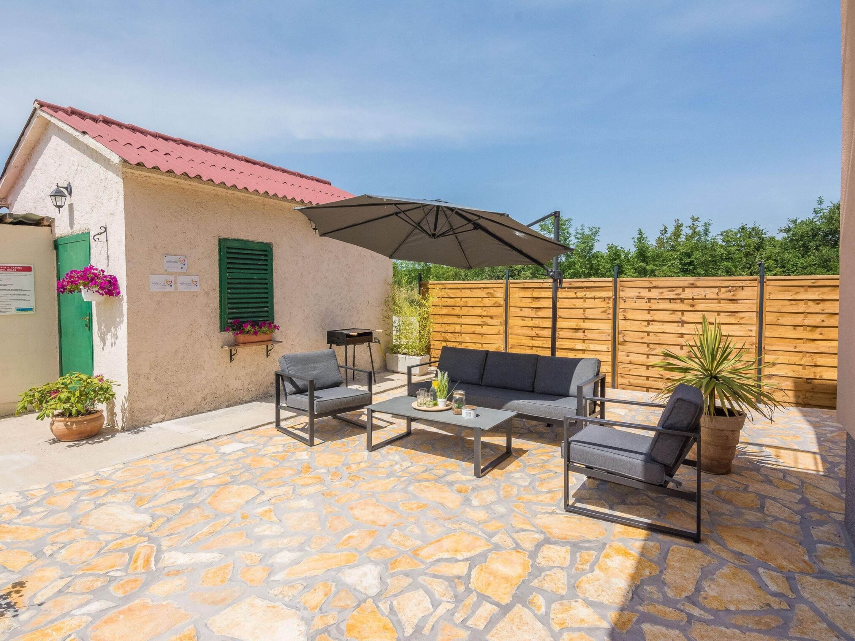Une terrasse extérieure avec un sol en pierre, une table avec des chaises, un canapé et un parasol.