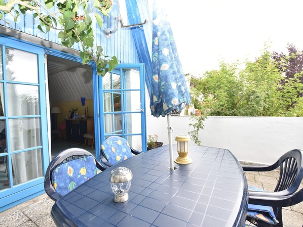 Ein blaues Haus mit einer gefliesten Terrasse, einem Tisch mit Stühlen und einem dekorativen Glasobjekt.