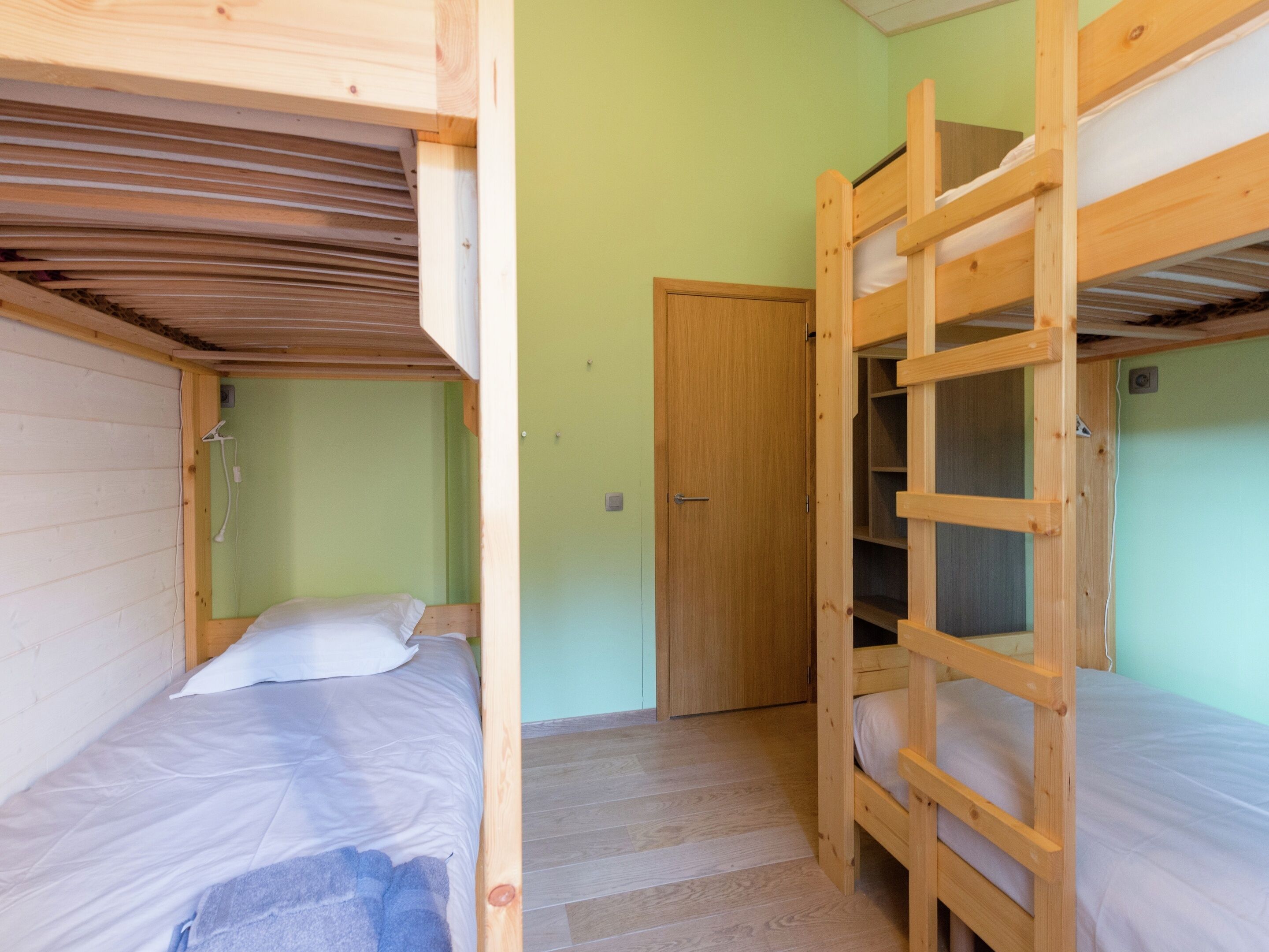Une pièce avec deux lits superposés, une porte en bois et un sol carrelé.