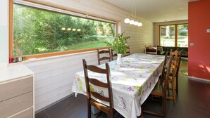 En matplats med ett bord dukat för fyra personer, trästolar, en vas med en växt och ett stort fönster med utsikt över träd.