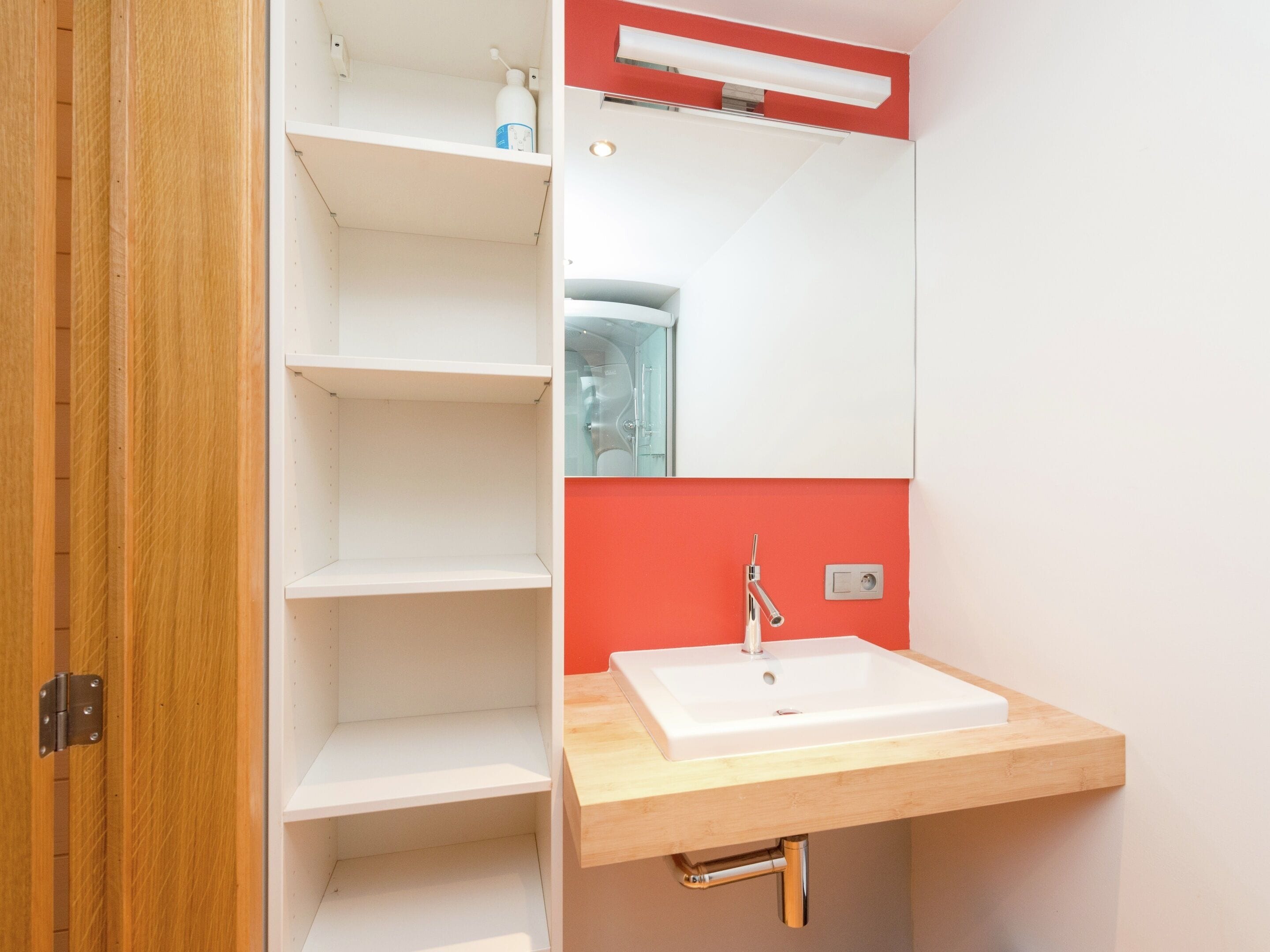 A bathroom with a white sink, a mirror, and a red accent wall.