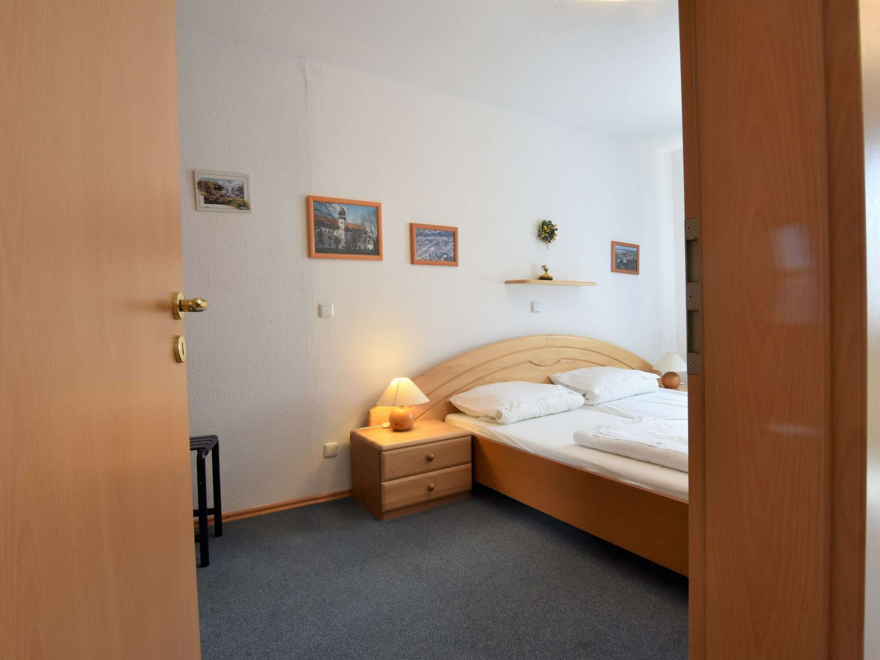 A bedroom with a wooden bed, a nightstand with a lamp, and a small dresser.