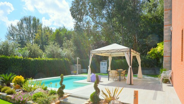 Un giardino sul retro con piscina, patio coperto e un piccolo orto con diverse piante e prato.