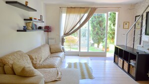 Un soggiorno con un divano color beige, un tavolino da caffè e una libreria. Una porta scorrevole in vetro dà accesso a un giardino.