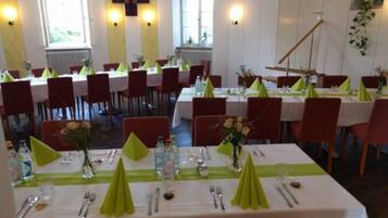 A dining area with tables set for service, chairs, and a cross on the wall.