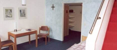 A bedroom with a bed, a desk, a chair, and a staircase leading to another room.
