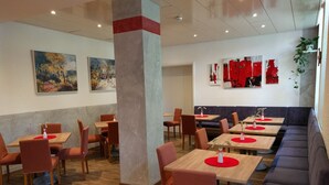 Un restaurant avec des tables et des chaises en bois, un canapé bleu et des touches de couleur rouge sur les murs.