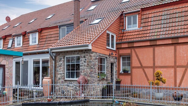 Una casa de estilo europeo tradicional con fachada de piedra, techo de tejas rojas y un pequeño estanque al frente.