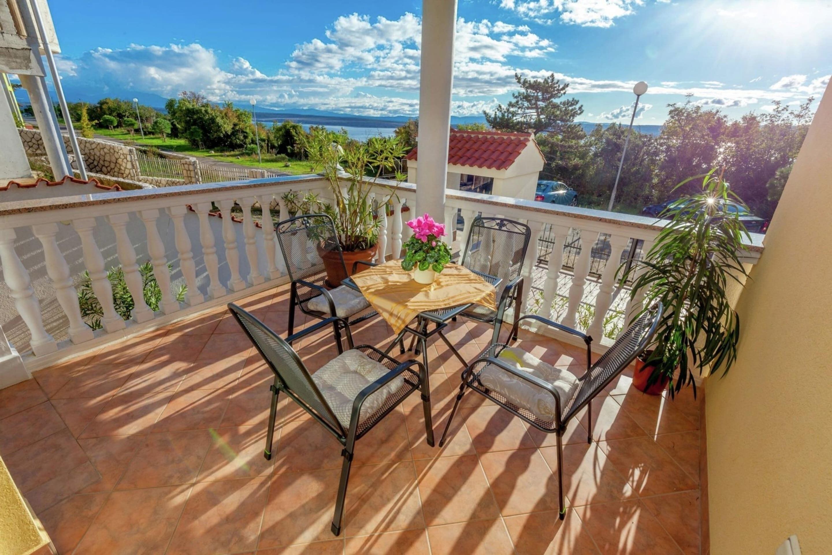A balcony with a table and chairs, potted plants, and a view of the sea.