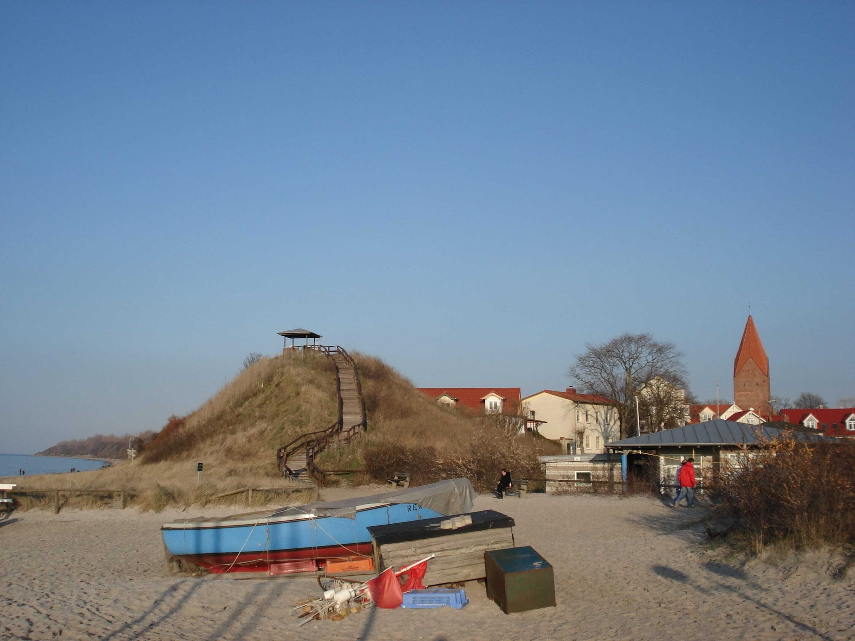 A beach with boats, a wooden staircase, and buildings in the background.