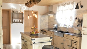 Een keuken met houten kastjes, een centraal eiland met krukken, een hanglamp en een raam met gordijnen.