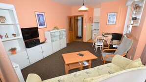Un salon comprenant un canapé, une table basse, un téléviseur et un coin cuisine visible à travers une porte ouverte.