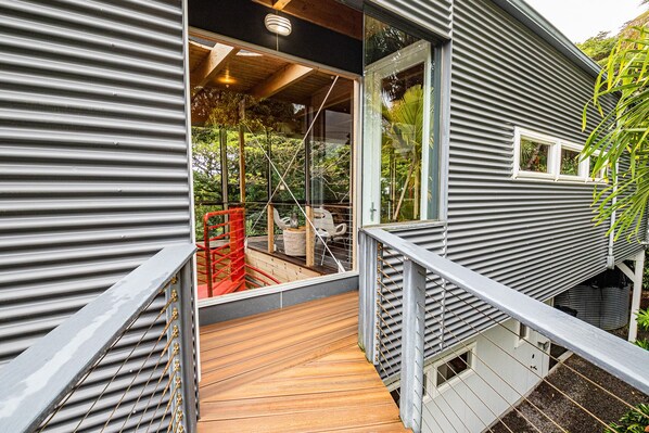 Una casa moderna con terraza de madera y puerta de vidrio que da a un espacio exterior cubierto.