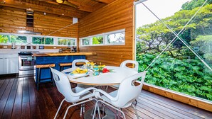 Eine moderne Küche mit Holzwänden, ein Essbereich mit weißen Stühlen und ein großes Fenster mit Blick auf einen üppigen Garten.