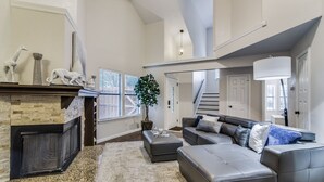 Una sala de estar amplia con chimenea, un sofá modular grande y una escalera que conduce a un nivel superior.