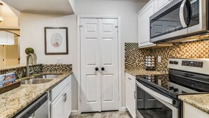 Una cocina con armarios blancos, puerta doble, microondas, horno y salpicadero de azulejos.