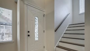 Una entrada limpia y moderna con una puerta blanca, una escalera de madera y piso alfombrado.