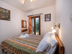 A hotel room with a bed, a bathroom mirror, a painting, an air conditioning unit, and a balcony with curtains. - Villa in Crete Near Beach and Olive Groves (Rethymno)