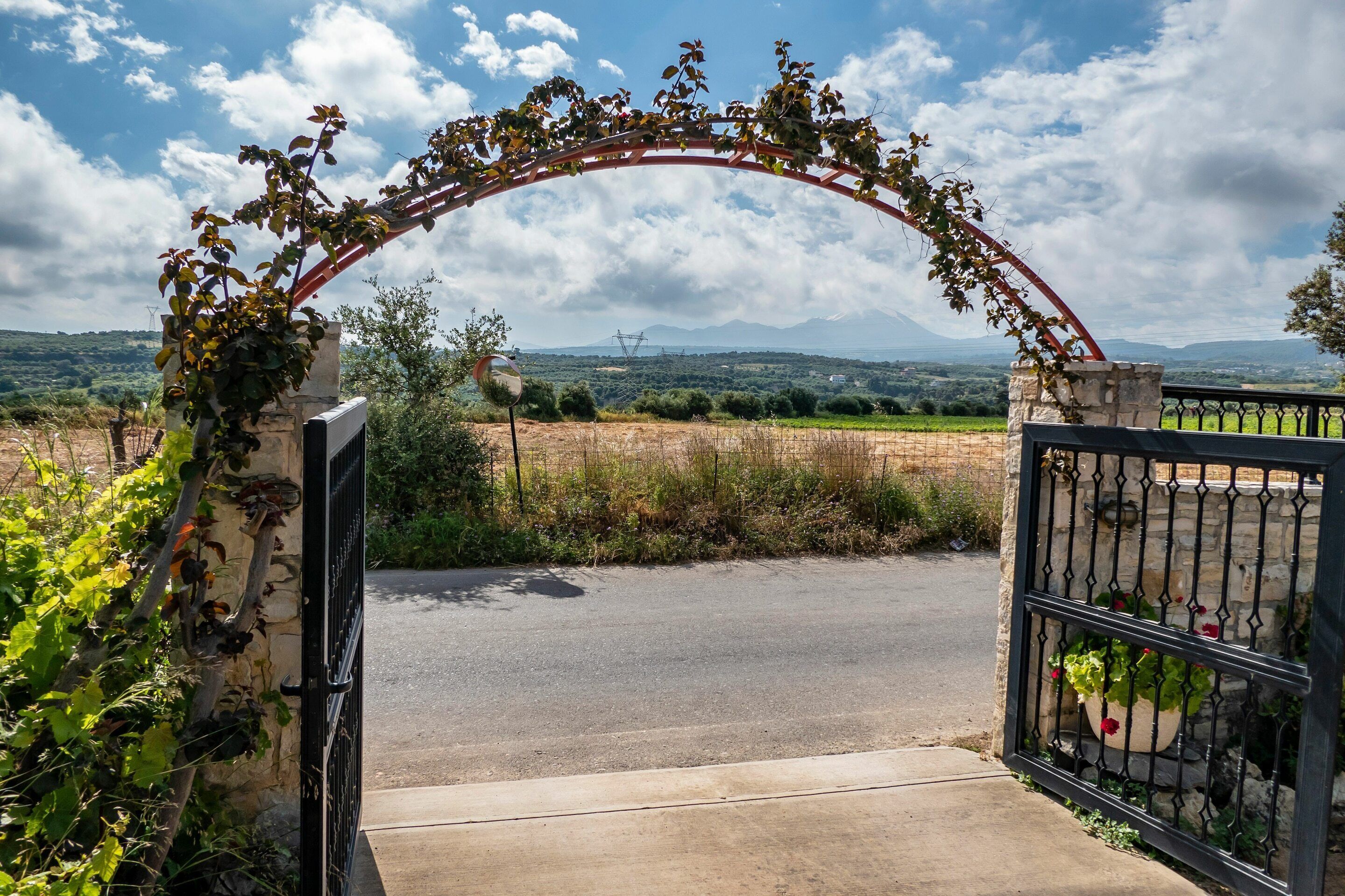 An open gate with a stone archway, leading to a paved road.
