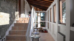 A staircase leading to a second floor with a wooden ceiling, stone walls, and large windows offering views of trees. - Tuscan Hideaway With Pool (San Casciano dei Bagni)