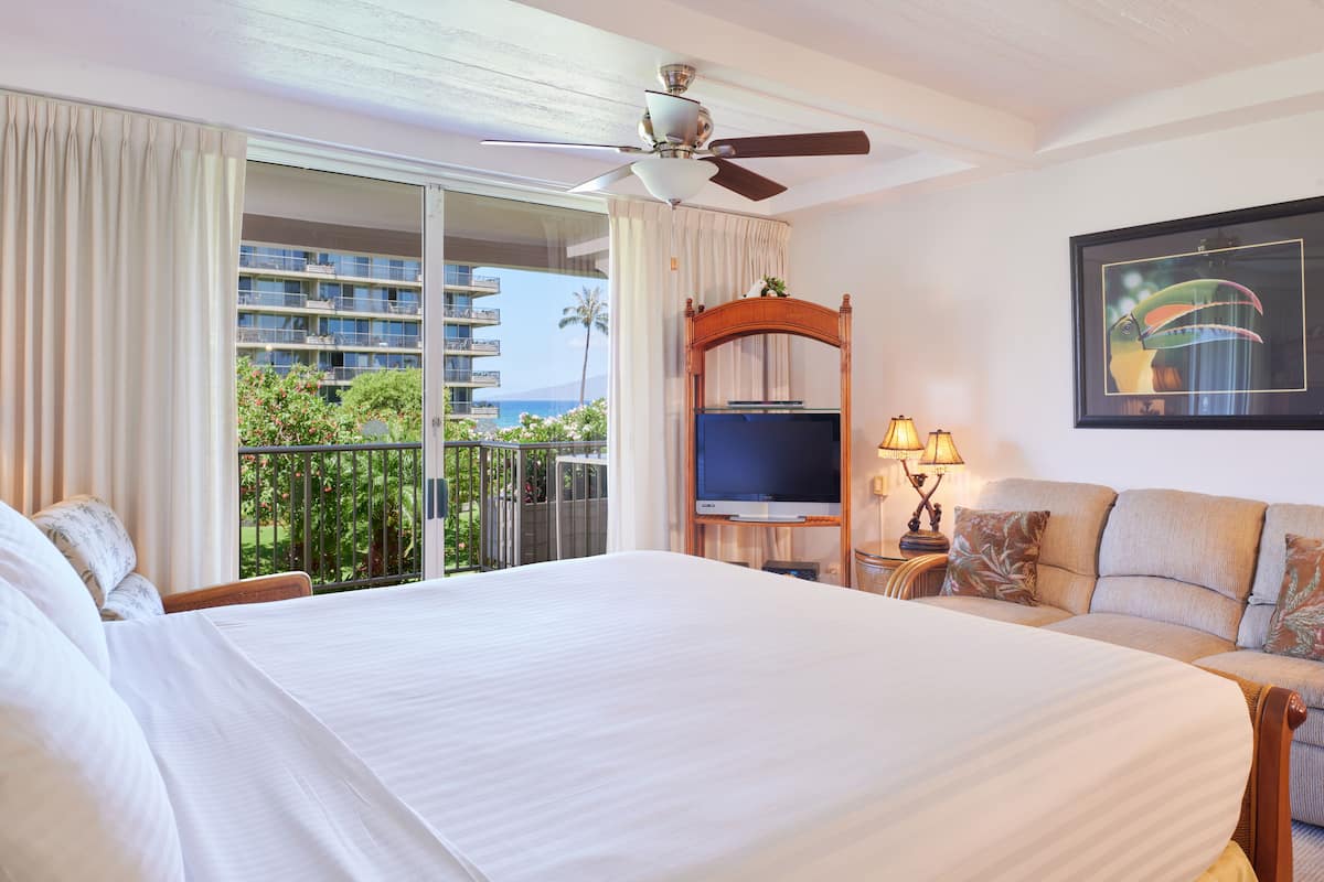 Une chambre d’hôtel avec un grand lit, une télévision, un balcon avec vue sur l’océan et un ventilateur de plafond.