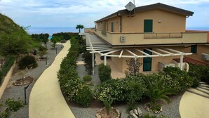 A building with a beige exterior, a covered outdoor area with a pergola, and a view of the sea. - Apartment in Tropea With Sea Views & Pool (Parghelia)