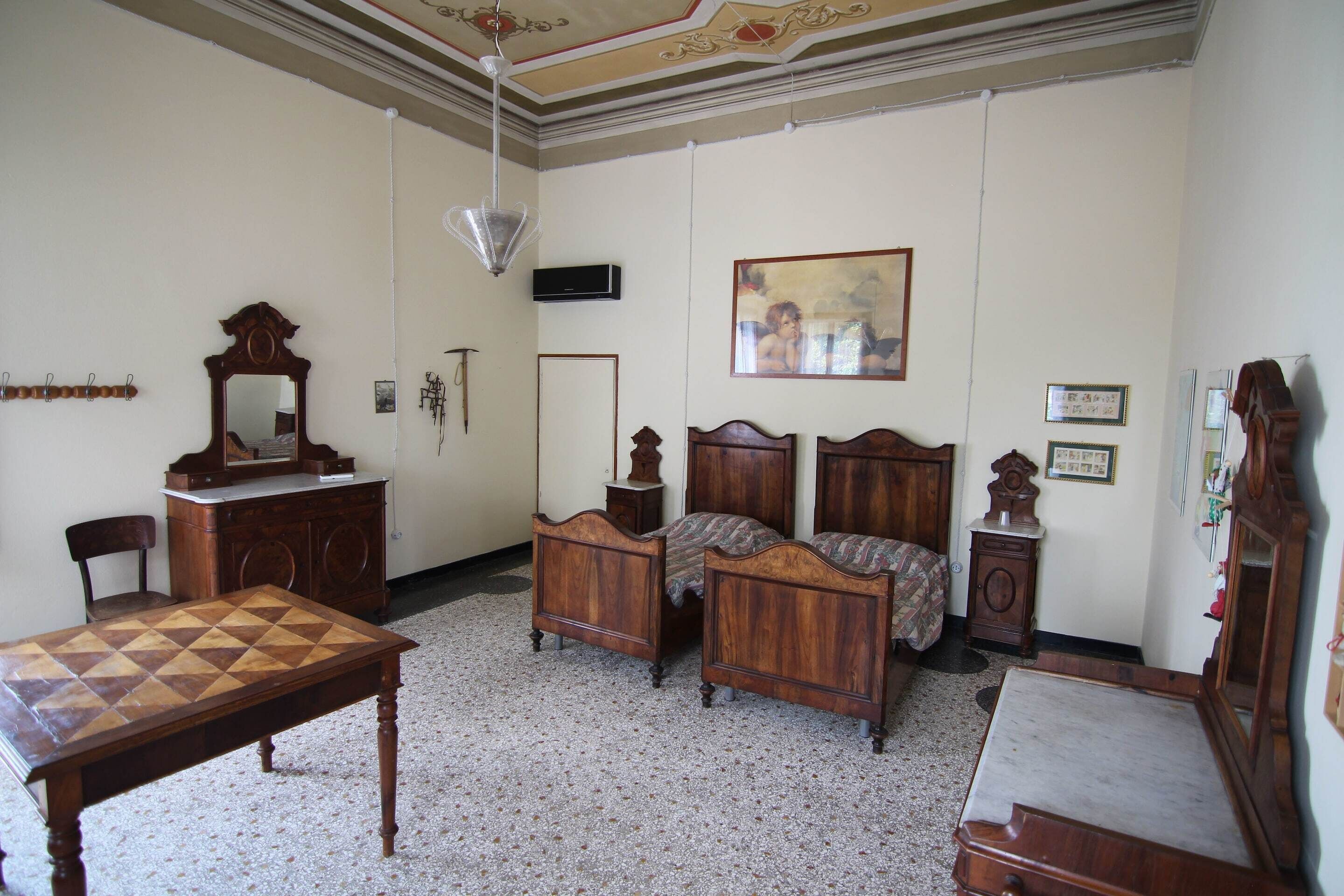 A room with a wooden bed, a wooden table, a chair, a desk with a mirror, and a painting on the wall.