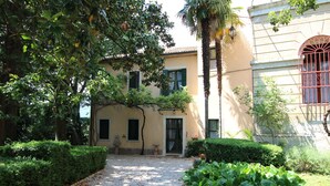 A courtyard with a gravel path, trimmed hedges, and a building with a door and windows. - Castle in Veneto With Garden & History (Romano d'Ezzelino)