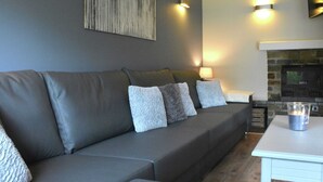 A modern living room with a grey sofa, a fireplace, and a table with a candle. - Luxurious Holiday Home in Hamoir With Terrace (Hamoir)
