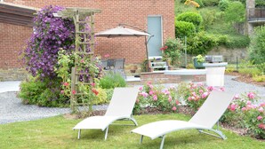 A garden with two lounge chairs, a wooden trellis with purple flowers, and a brick building in the background. - Luxurious Holiday Home in Hamoir With Terrace (Hamoir)