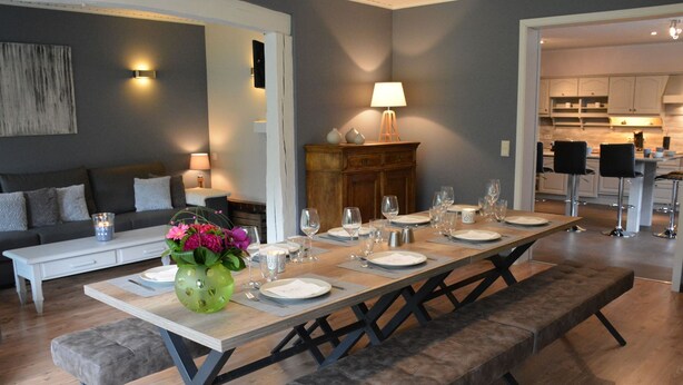 A dining area with a long table set for six, benches, a sofa, and a cabinet with a lamp. - Luxurious Holiday Home in Hamoir With Terrace (Hamoir)