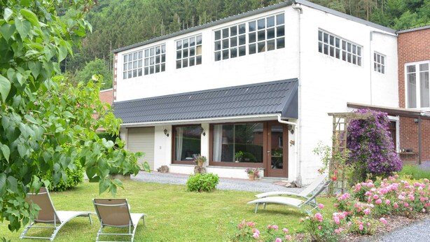 A two-story building with a white facade and a dark roof, surrounded by a well-maintained garden with pink flowers and two lounge chairs. - Luxurious Holiday Home in Hamoir With Terrace (Hamoir)