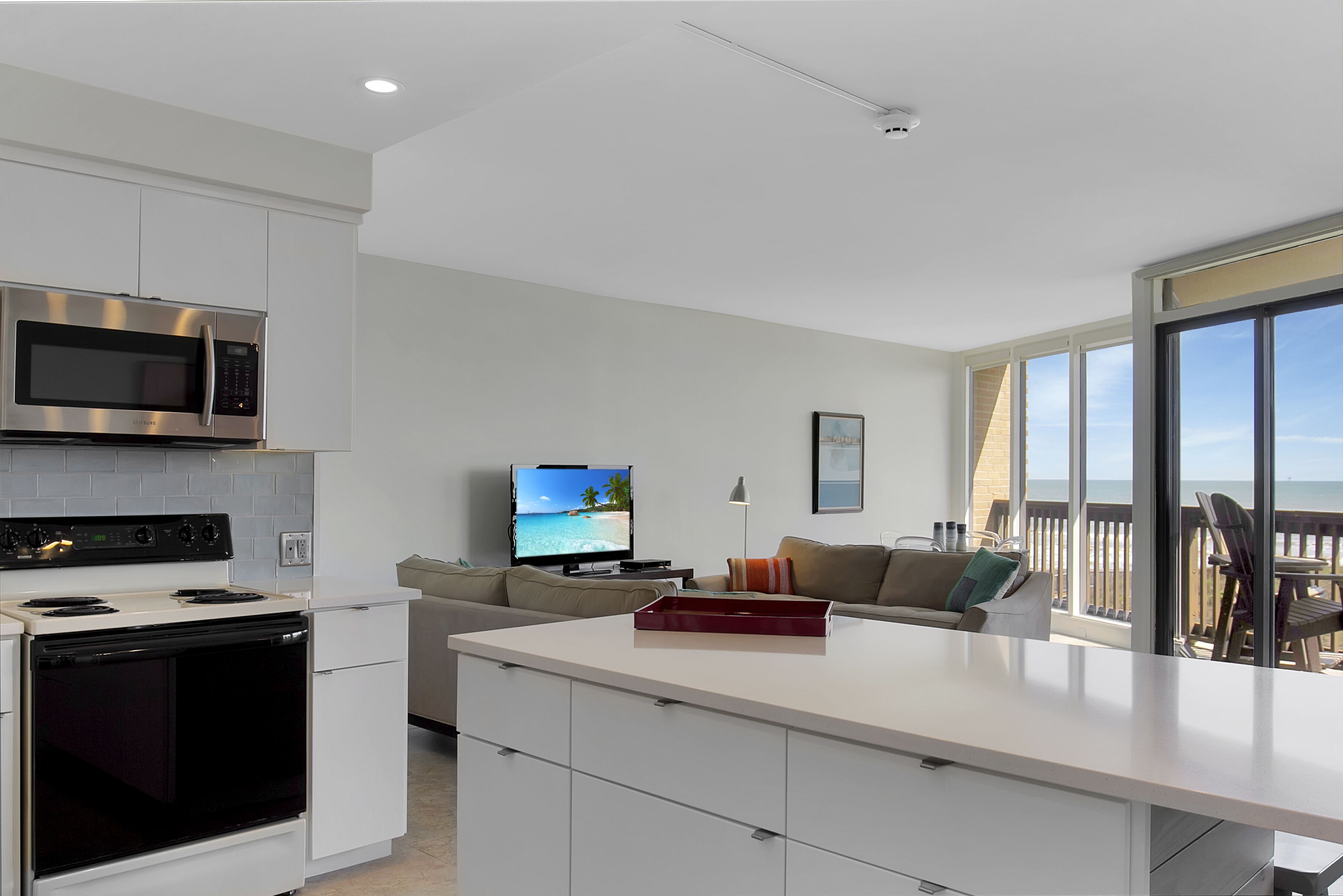 A modern kitchen with a built-in microwave, stove, and oven. There is a dining area with a large window overlooking a balcony.