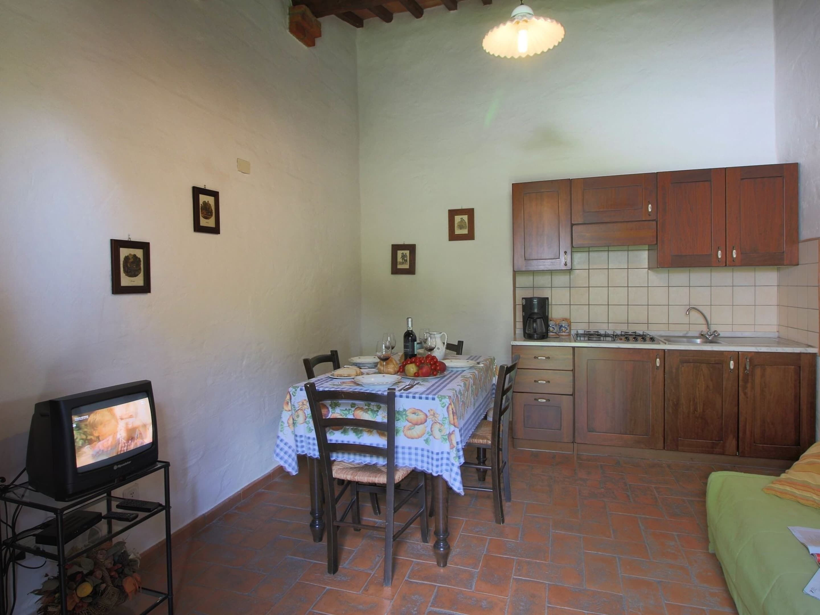 A compact kitchen with wooden cabinets, a tiled backsplash, and a dining area with a table set for two.