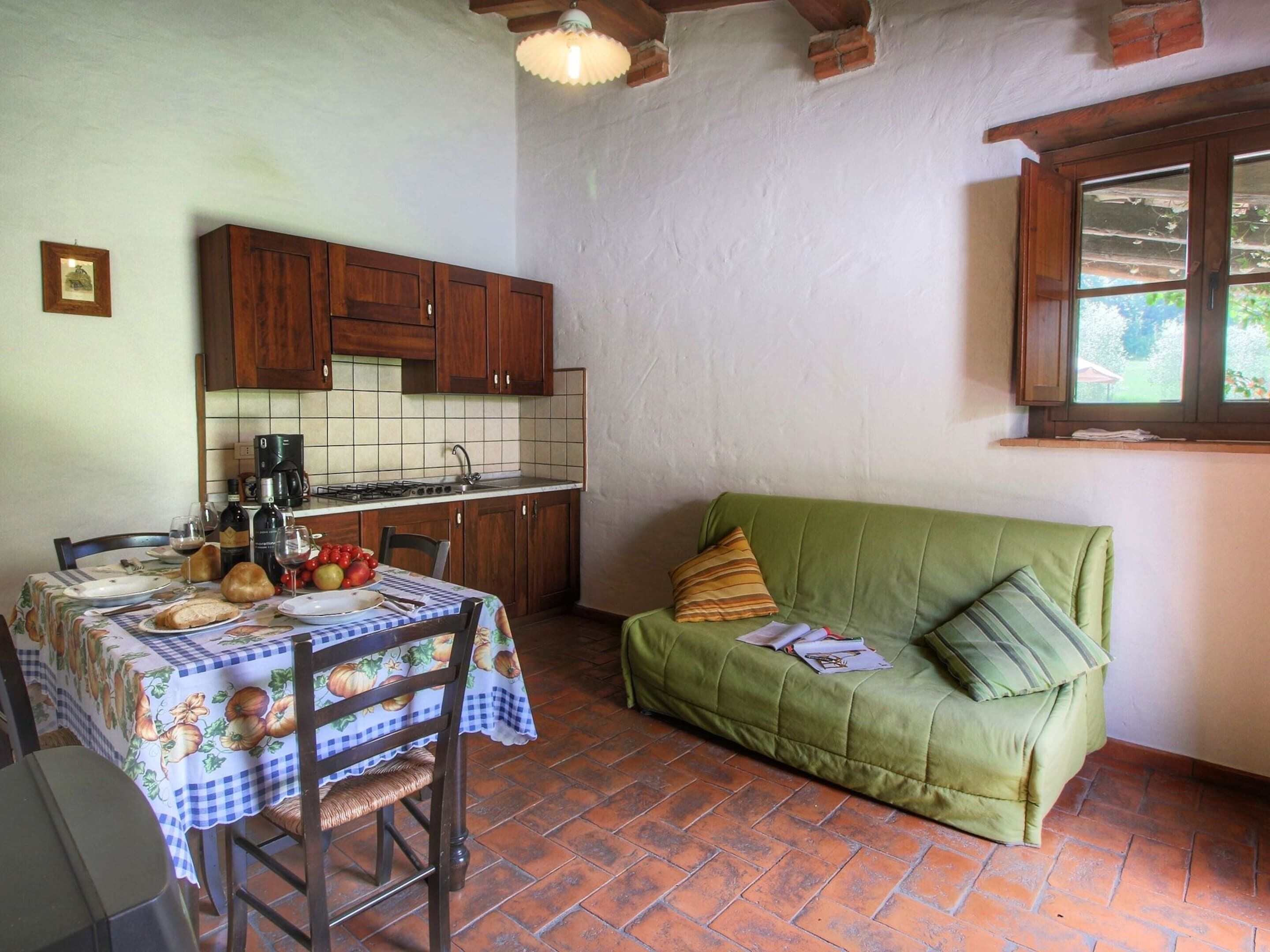 A compact kitchen with wooden cabinets, a tiled backsplash, and a green sofa with cushions.