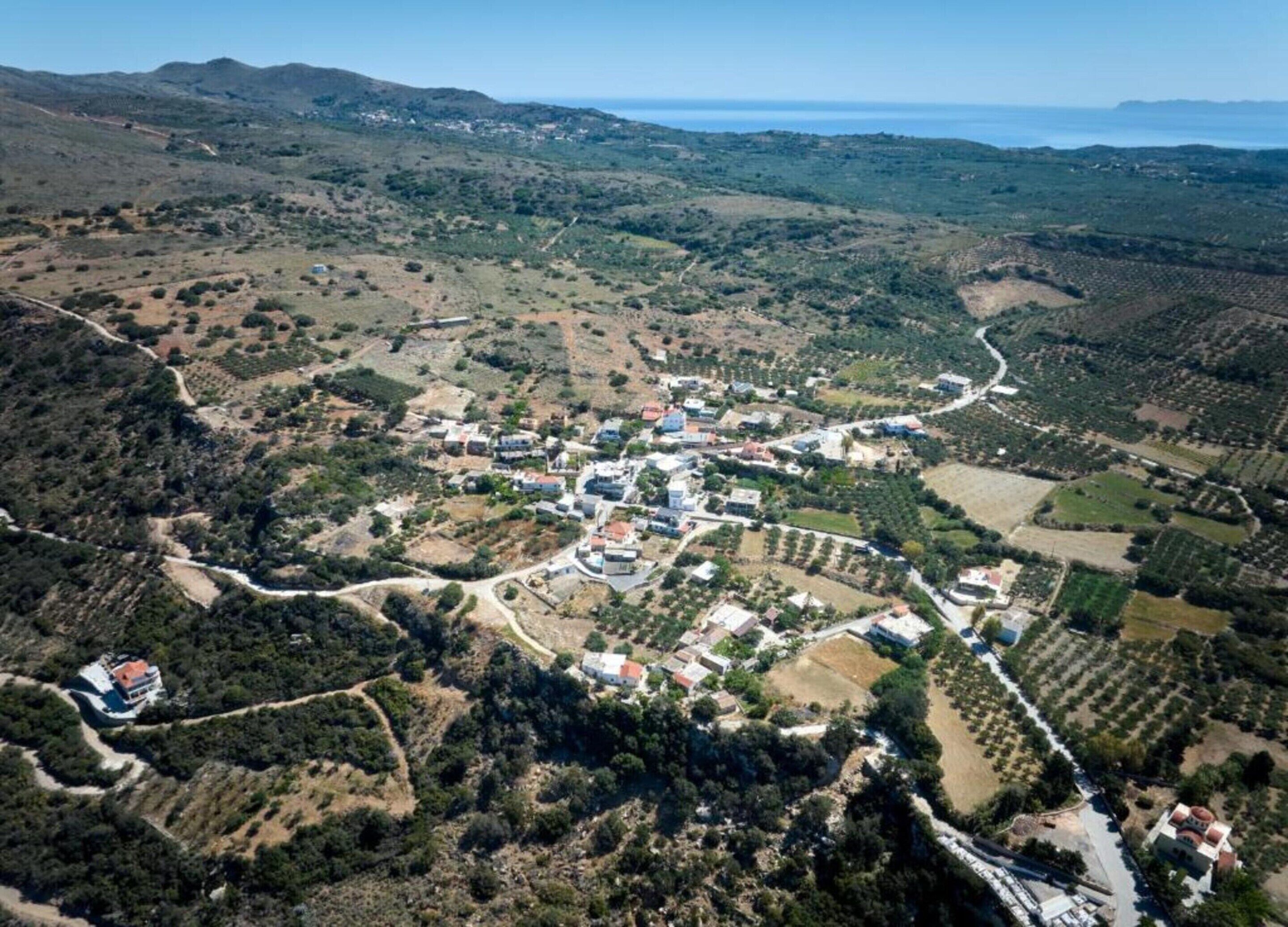 An aerial view of a coastal village with houses, a winding road, and agricultural fields.